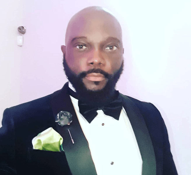 Man in tuxedo with a bow tie and pocket square posing against a light background.