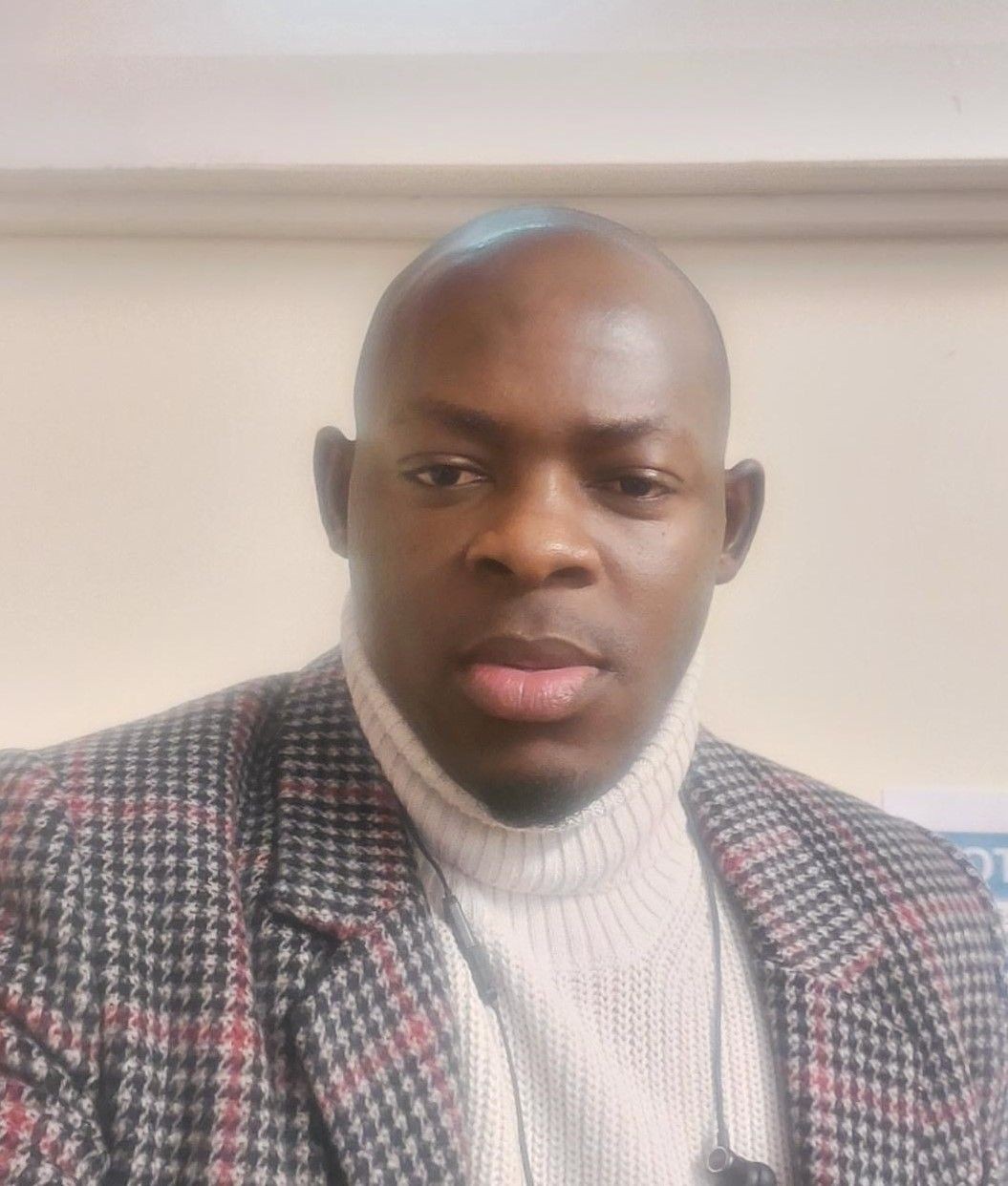 Person wearing a checkered jacket and white turtleneck sweater indoors.