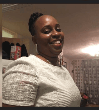 Person wearing a textured white blouse, standing indoors with shelves and a lit room in the background.