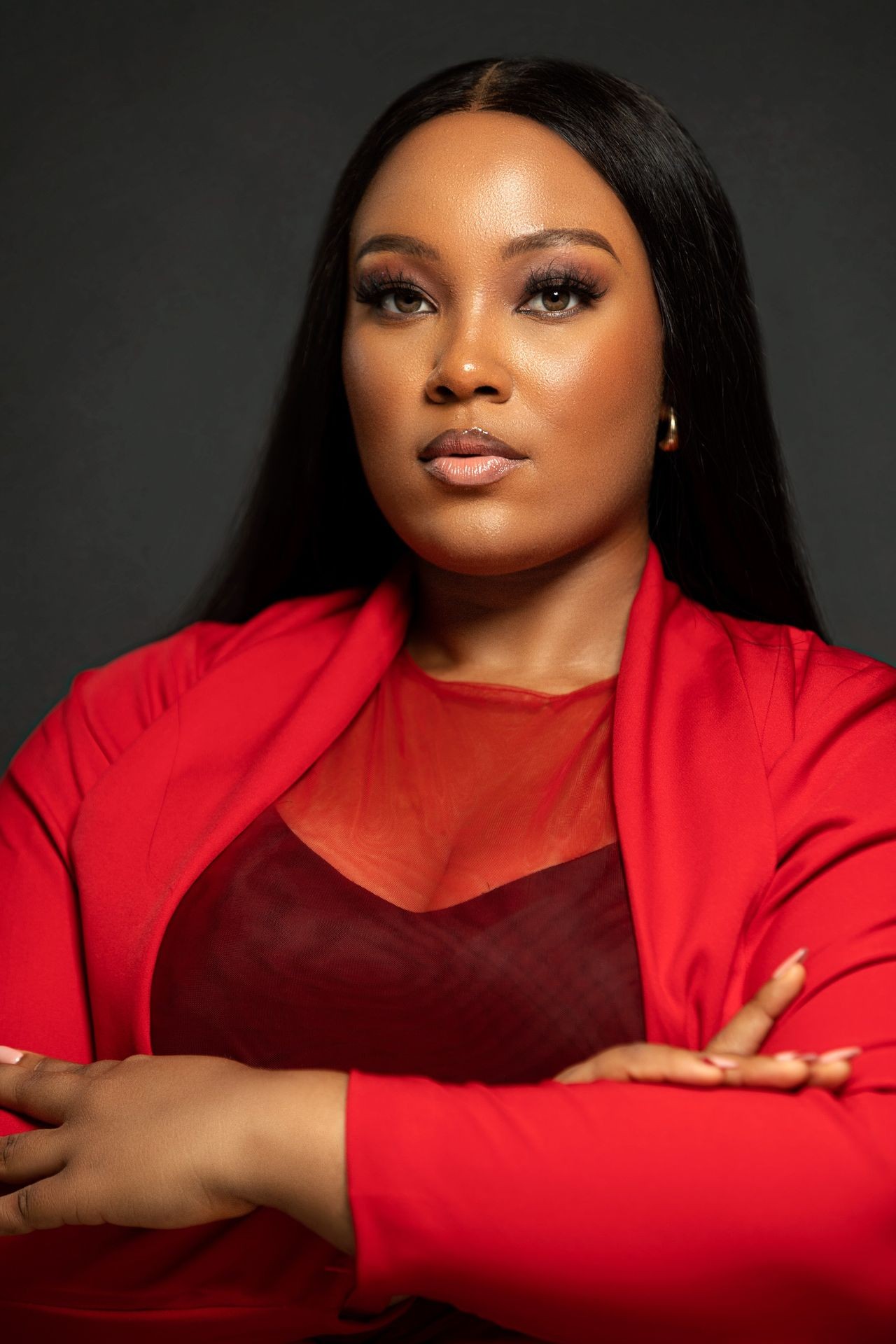 Confident woman in a red outfit with crossed arms against a dark backdrop.